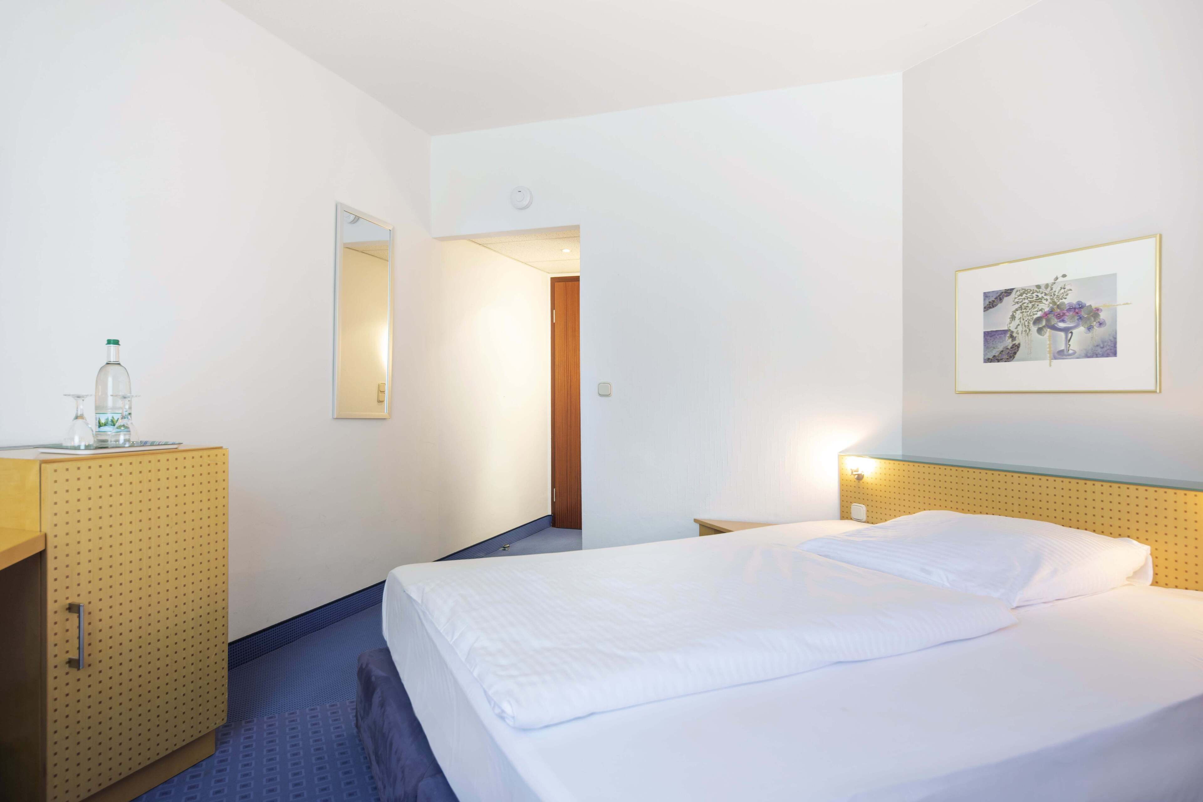 Ein Hotelzimmer mit Bett, Schrank, Spiegel und einem gerahmten Bild an der Wand.