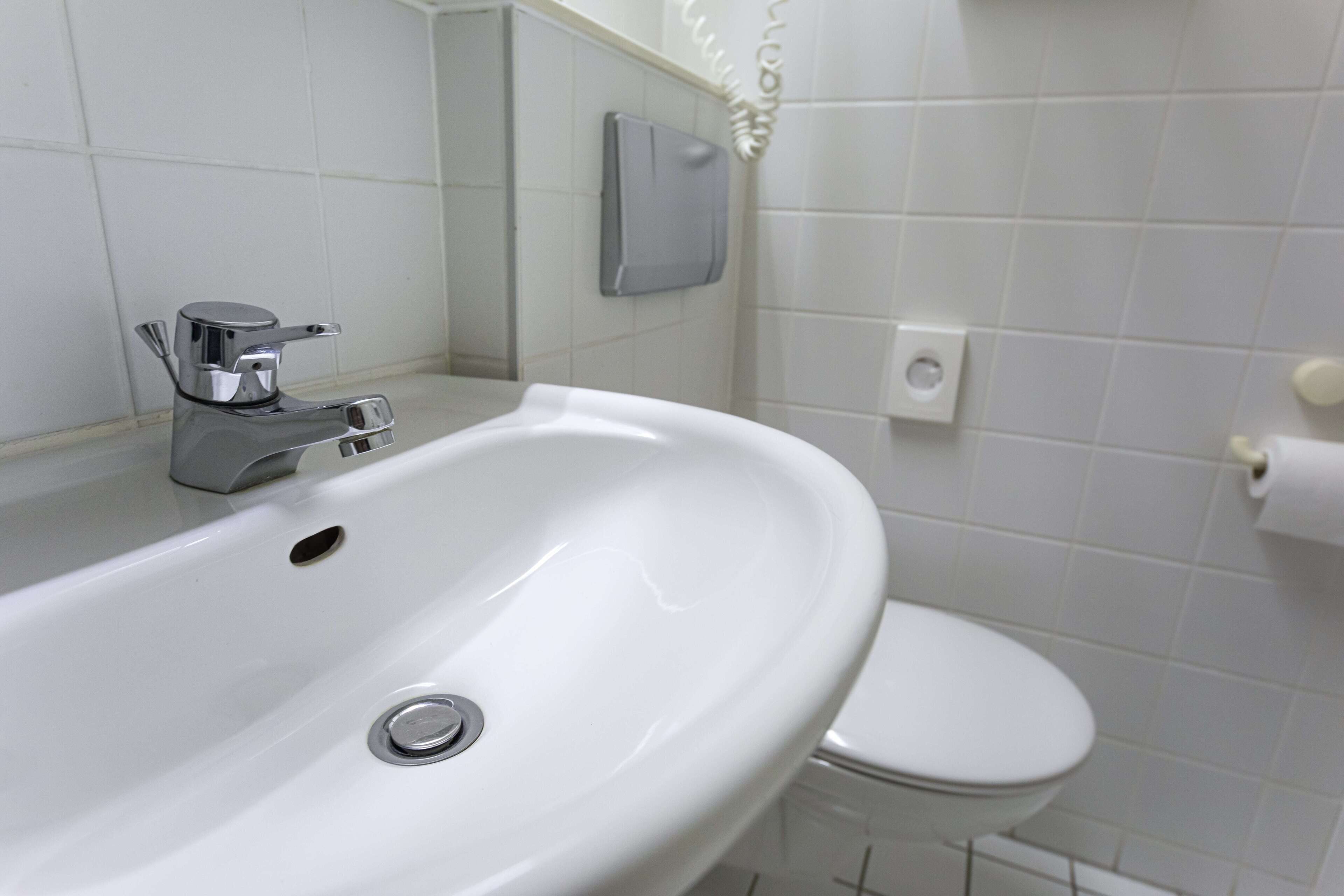 A bathroom with a white sink, a toilet, and a soap dispenser on the wall.