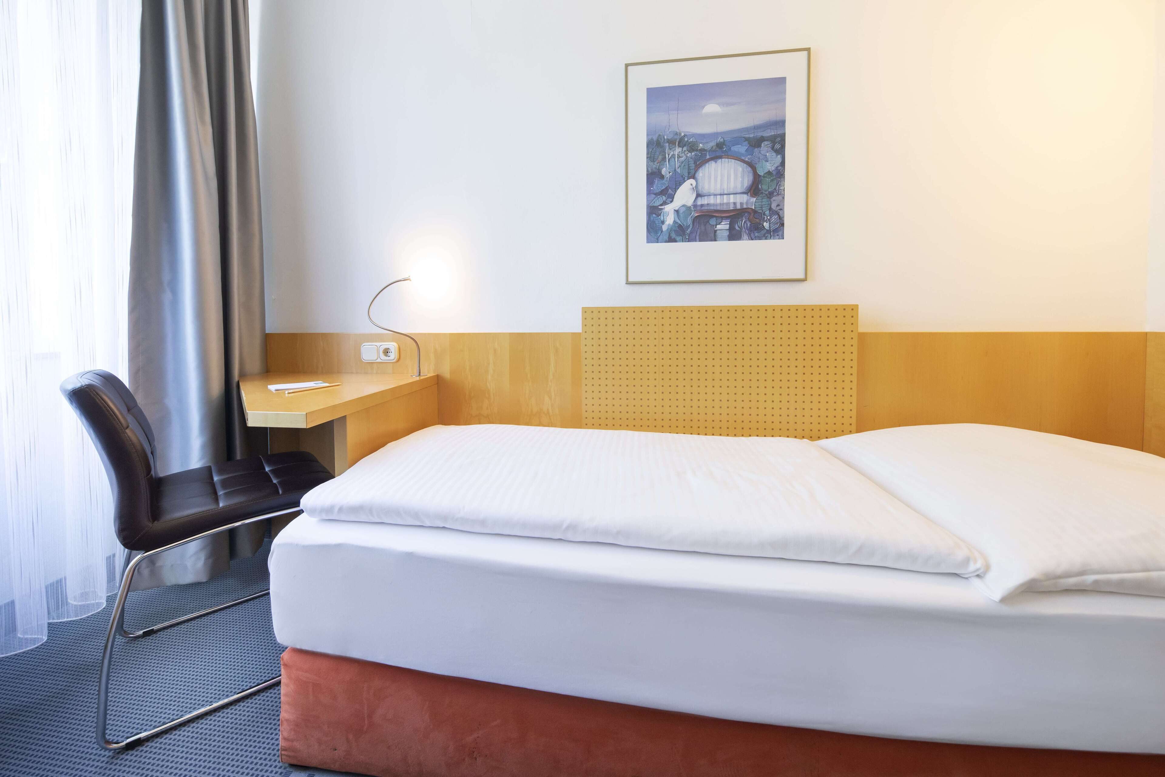 Ein Hotelzimmer mit Bett, Schreibtisch, Stuhl und einem gerahmten Bild an der Wand.