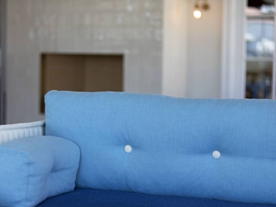 Un sofá azul con botones blancos, un cojín blanco y una silla blanca en una habitación con chimenea y estantería.