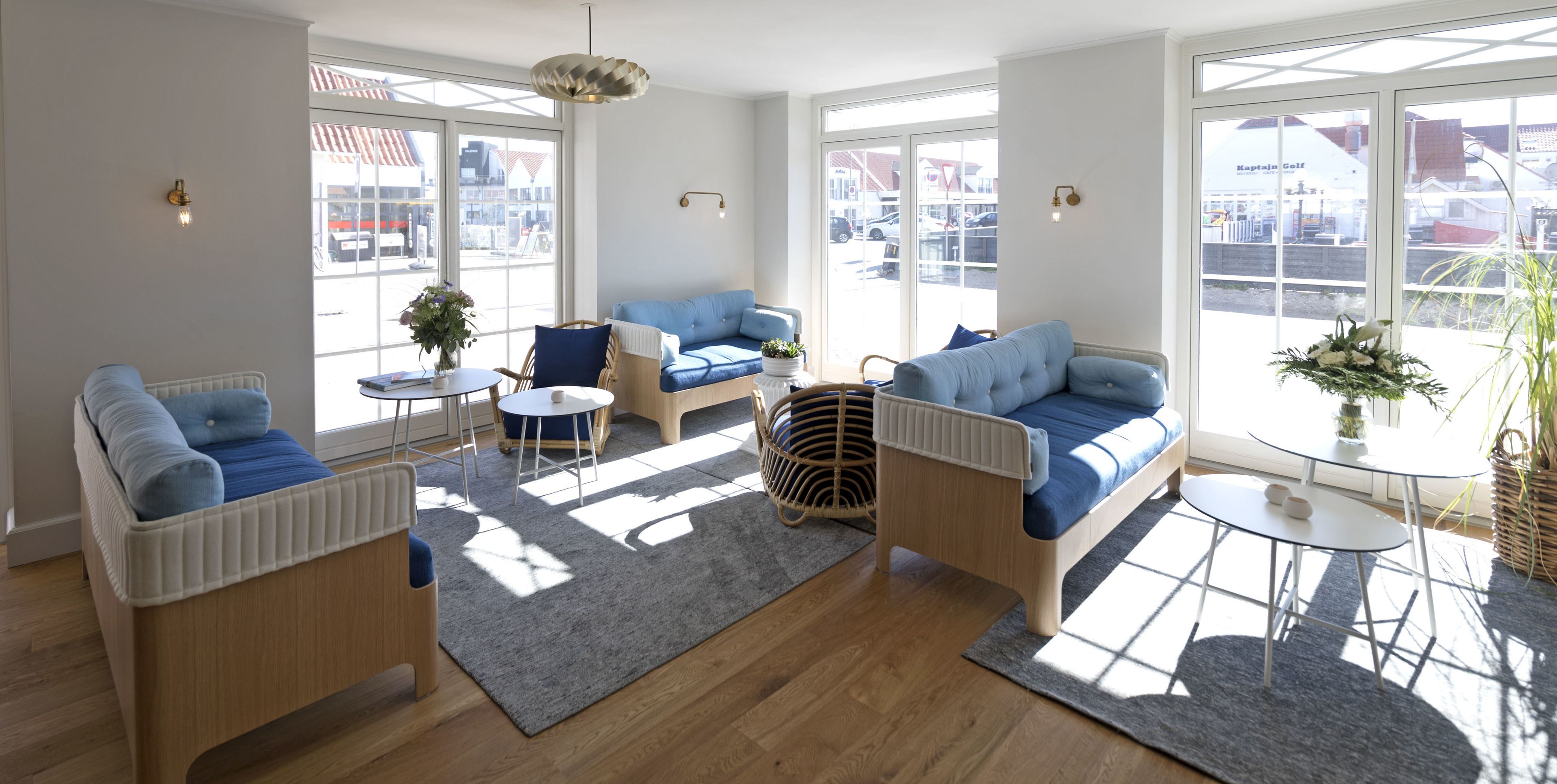 Ein helles Wohnzimmer mit einem blauen Sofa, einem Holztisch und einem Korbstuhl.
