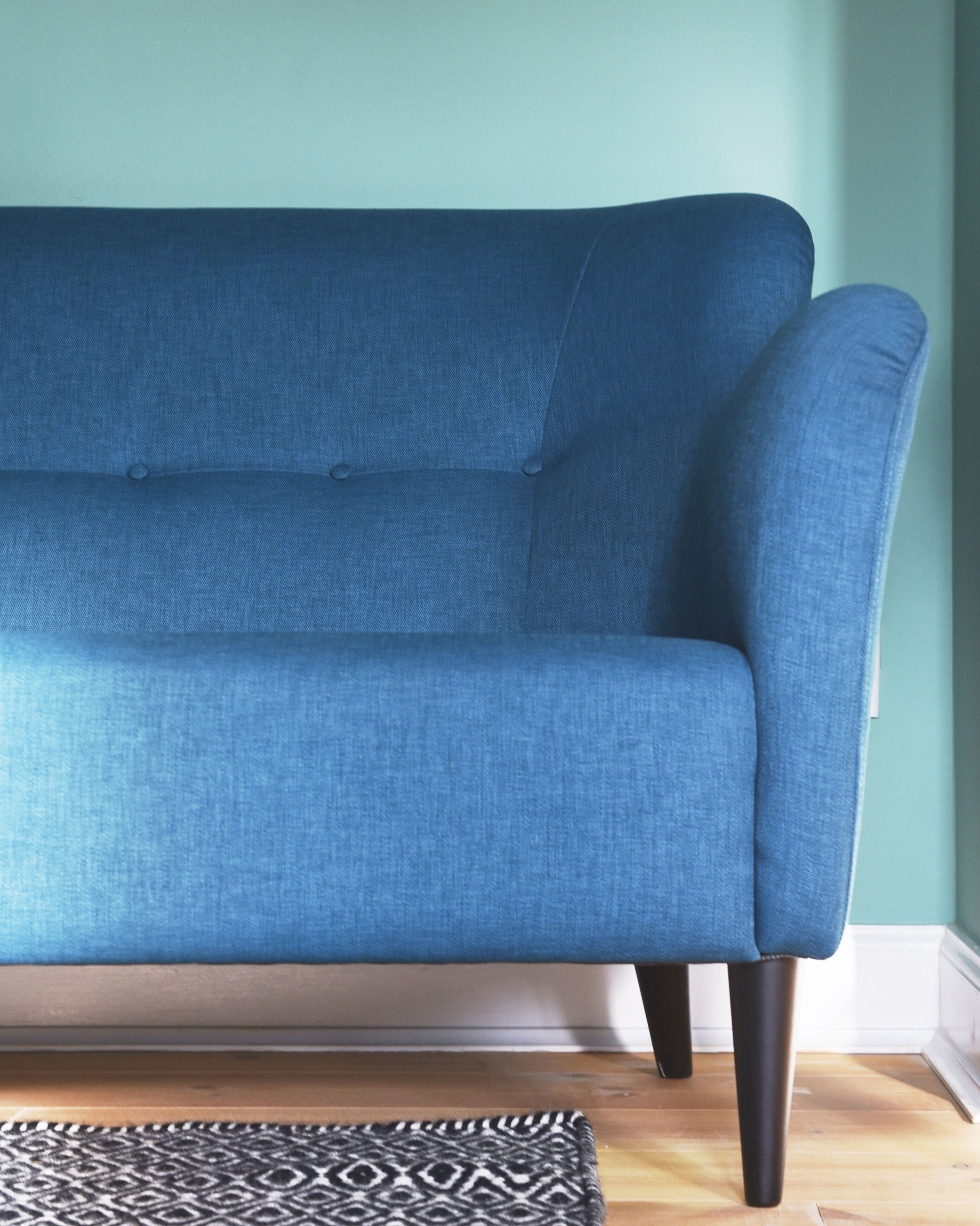 A blue sofa with a patterned rug in front.