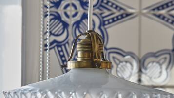 A hanging light fixture with a clear glass shade and a brass base, set against a wall with blue and white patterned tiles.