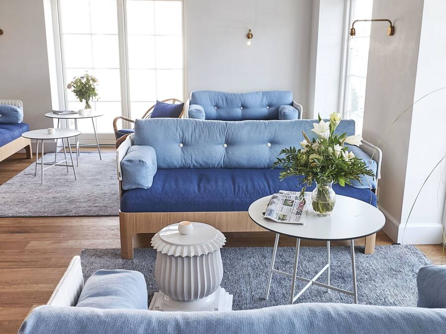 Una sala moderna con un sofá azul, una mesa de centro blanca y un jarrón de flores.