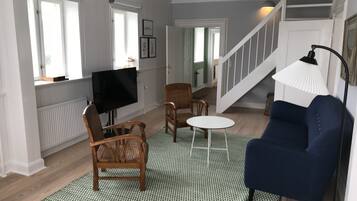 Ein Wohnzimmer mit Fernseher, zwei Holzstühlen, einem blauen Sofa, einem kleinen runden Tisch und einer Treppe.