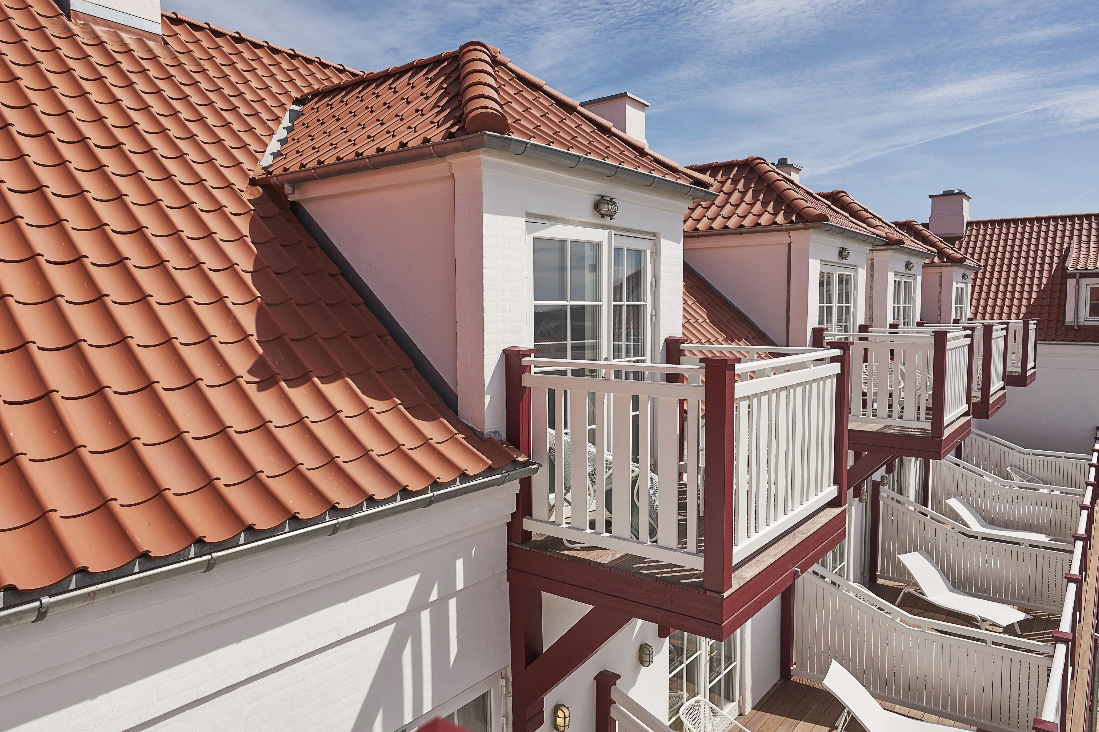 A residential building with terracotta tiled roofs, white exterior walls, and a balcony with white railings.