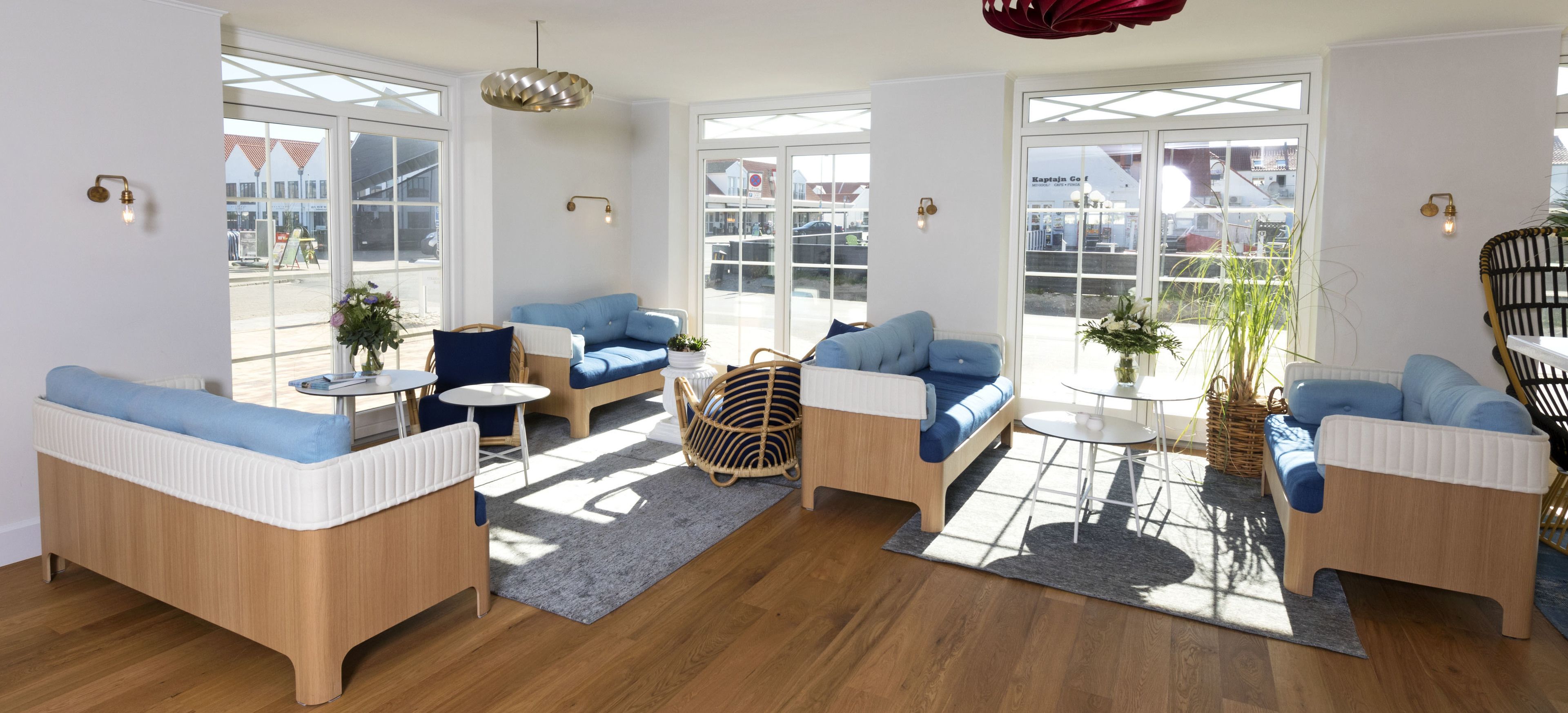 A spacious living area with large windows, blue sofas, a round coffee table, and a hanging light fixture.