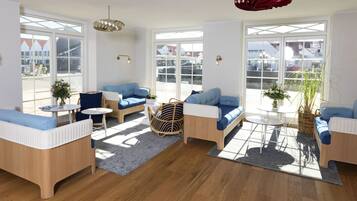 A spacious living area with large windows, blue sofas, a round coffee table, and a hanging light fixture.