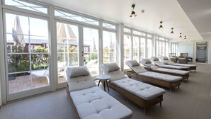 A sunlit room with large windows, multiple sun loungers, and a small table. - Strandhotellet - Blokhus (Blokhus)