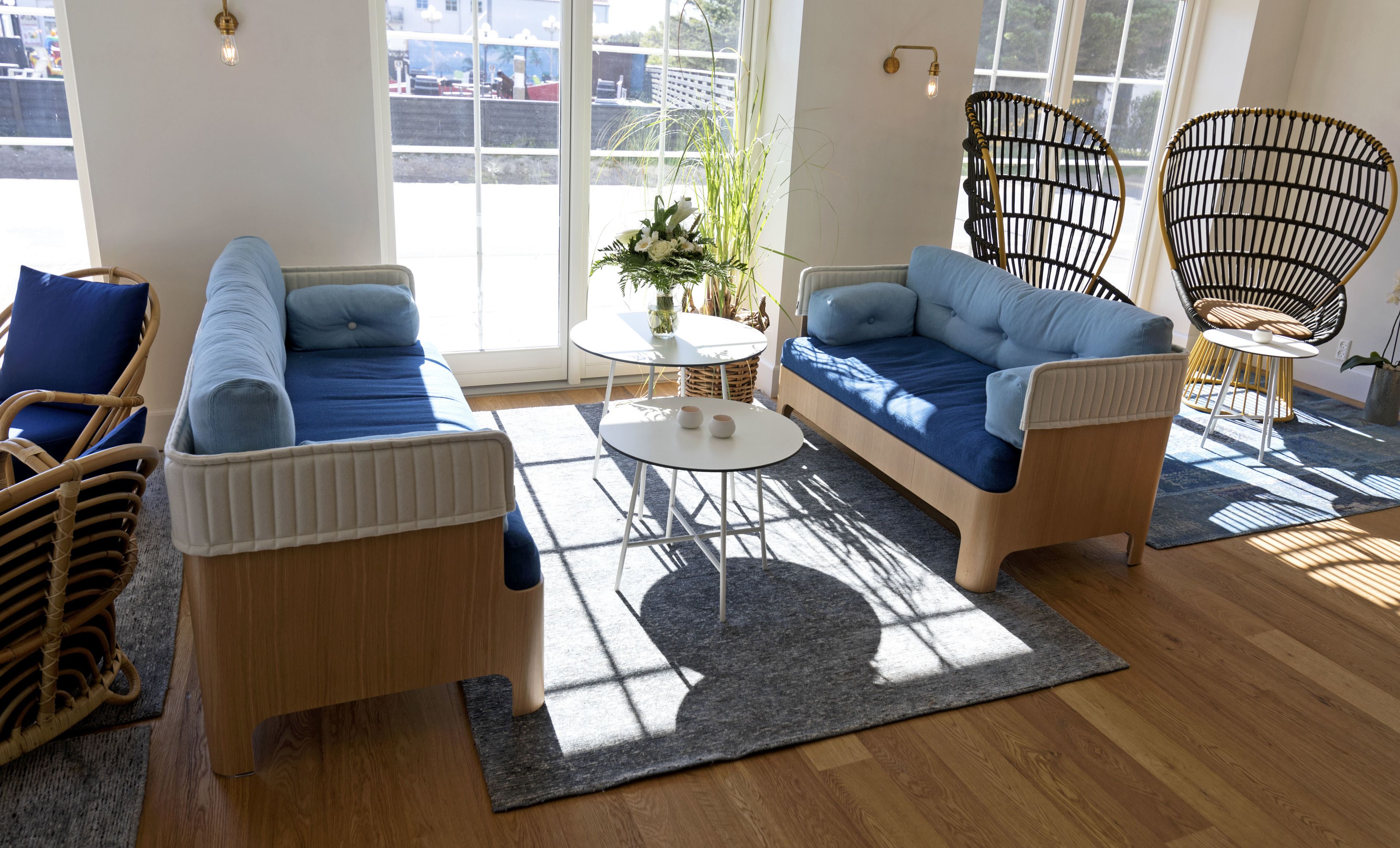 Een moderne woonkamer met een bank, rieten stoelen en een kleine tafel met een bloevas.