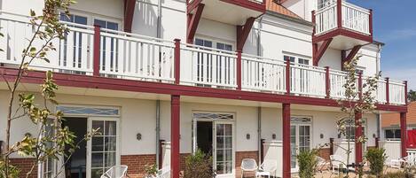 Un edificio de varios pisos con balcones, un patio cubierto con mobiliario exterior y un jardín bien cuidado.
