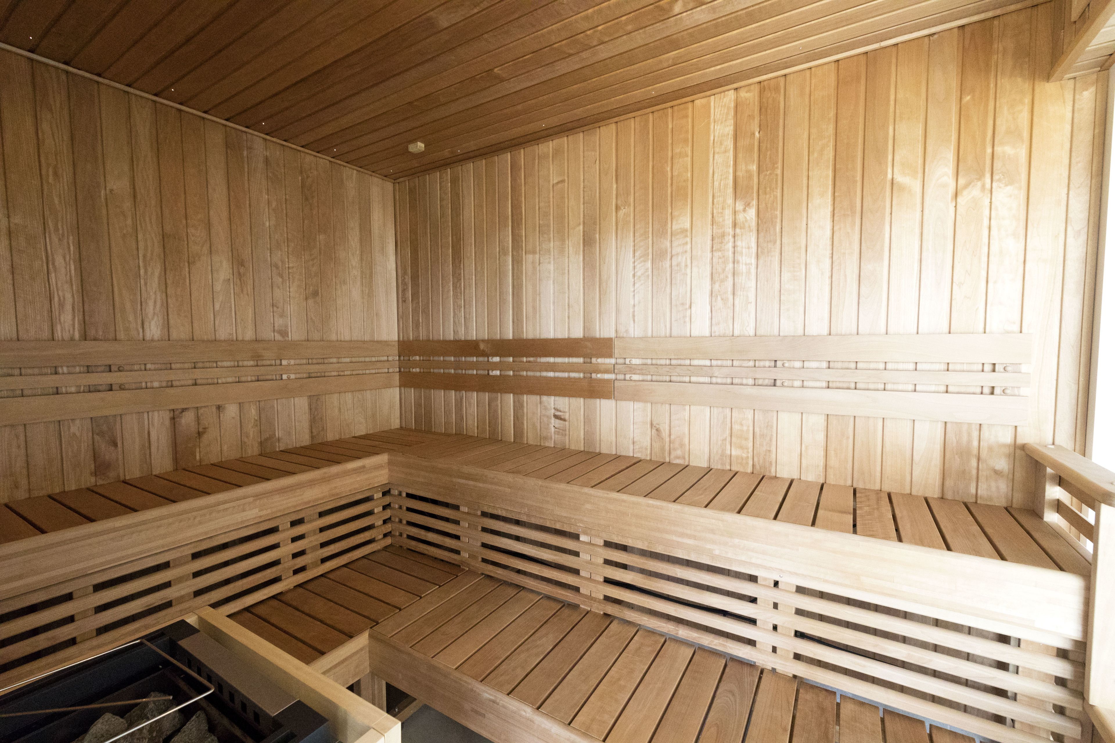 A sauna with wooden benches and a slatted floor, wooden walls, and a ceiling with horizontal beams.