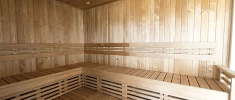 A sauna with wooden benches and a slatted floor, wooden walls, and a ceiling with horizontal beams.