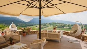 Une terrasse dotée de meubles en osier, d’une table en verre et d’un fauteuil suspendu offrant une vue sur la campagne.