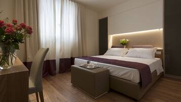 Une chambre d’hôtel moderne avec un grand lit, une table de chevet sur laquelle se trouve une assiette de biscuits, un vase de fleurs et un fauteuil.