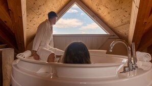 Une pièce mansardée en bois, avec un puits de lumière, une baignoire et une personne assise près de la fenêtre.