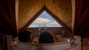 Une baignoire avec un puits de lumière au-dessus, deux personnes se détendant, et un plafond en bois.