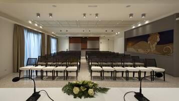 A conference room with rows of chairs, a podium with microphones, and a floral arrangement.