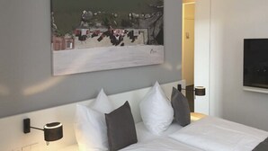 Un lit bien fait, avec une literie blanche et grise, un tableau accroché au mur et une table de chevet avec une lampe.