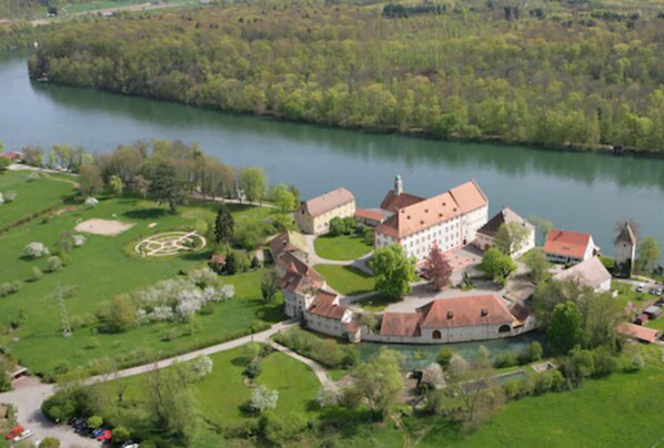 Eine Vogelperspektive auf einen historischen Landsitz mit einem großen Hauptgebäude, einem kreisförmigen Garten und einem Fluss.
