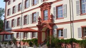 Un immeuble à plusieurs étages, doté d’une façade symétrique, de grandes fenêtres avec volets et d’une entrée centrale surmontée d’un arc décoratif.