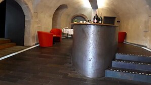 Un espace bar doté d’un grand comptoir en métal, de chaises rouges et d’une table recouverte d’une nappe blanche.
