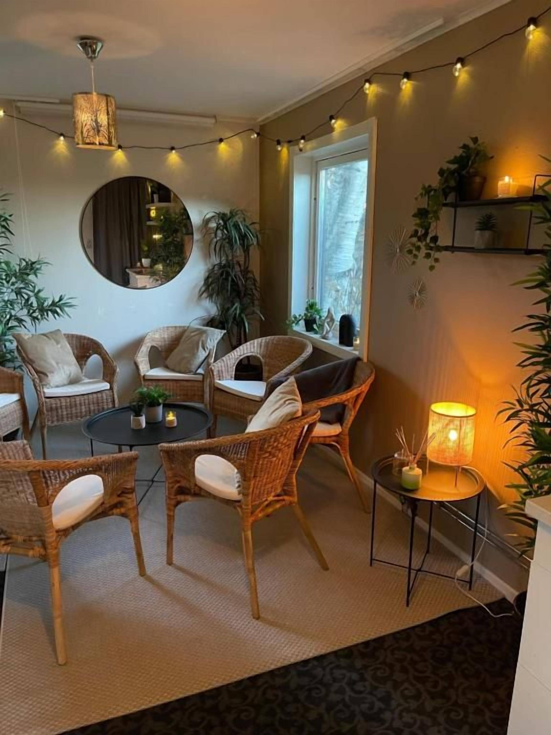 A cozy room with wicker furniture, a round mirror, and string lights.