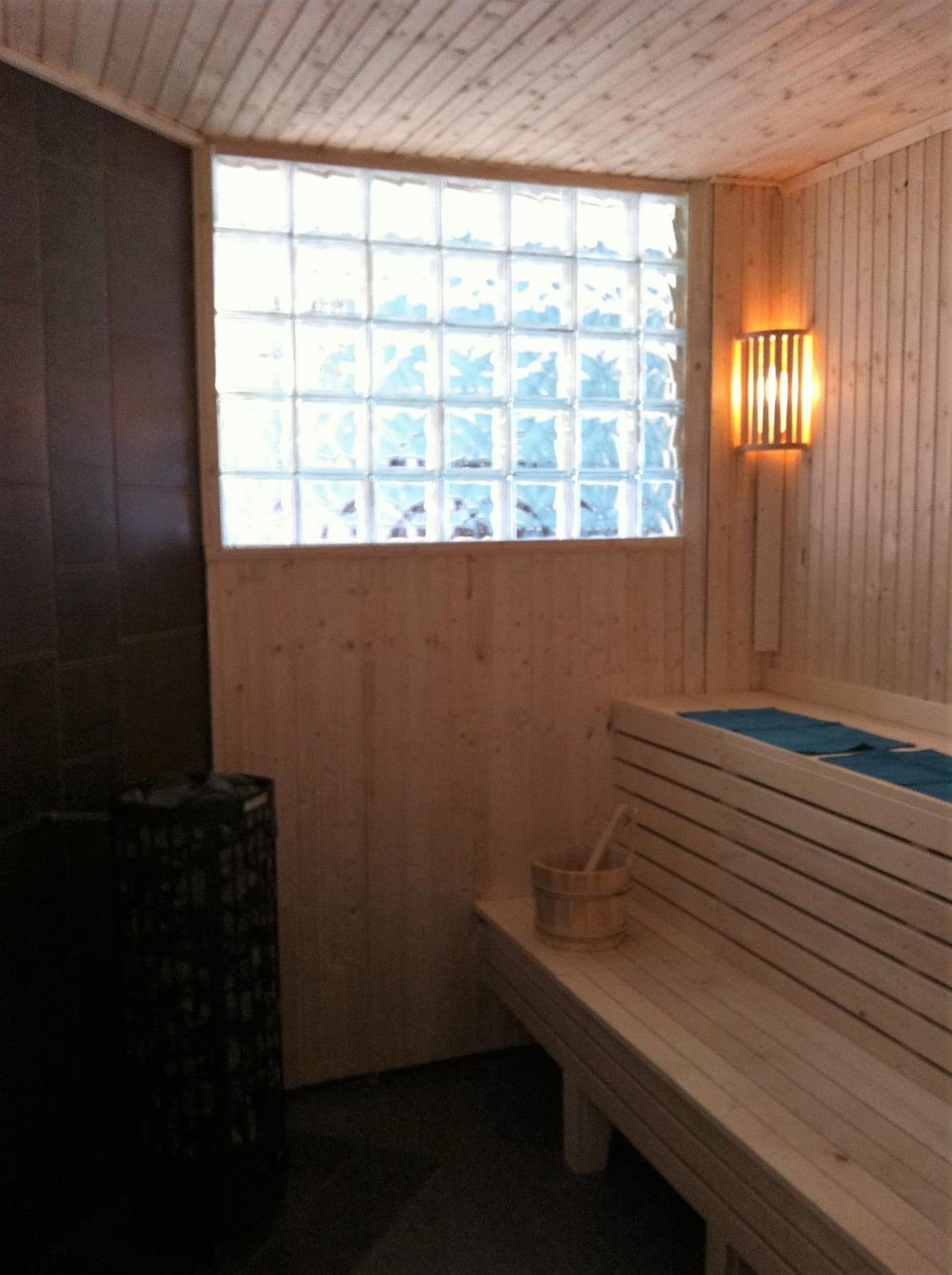 A sauna room with a wooden bench, a window with a view, and a wall-mounted light fixture.