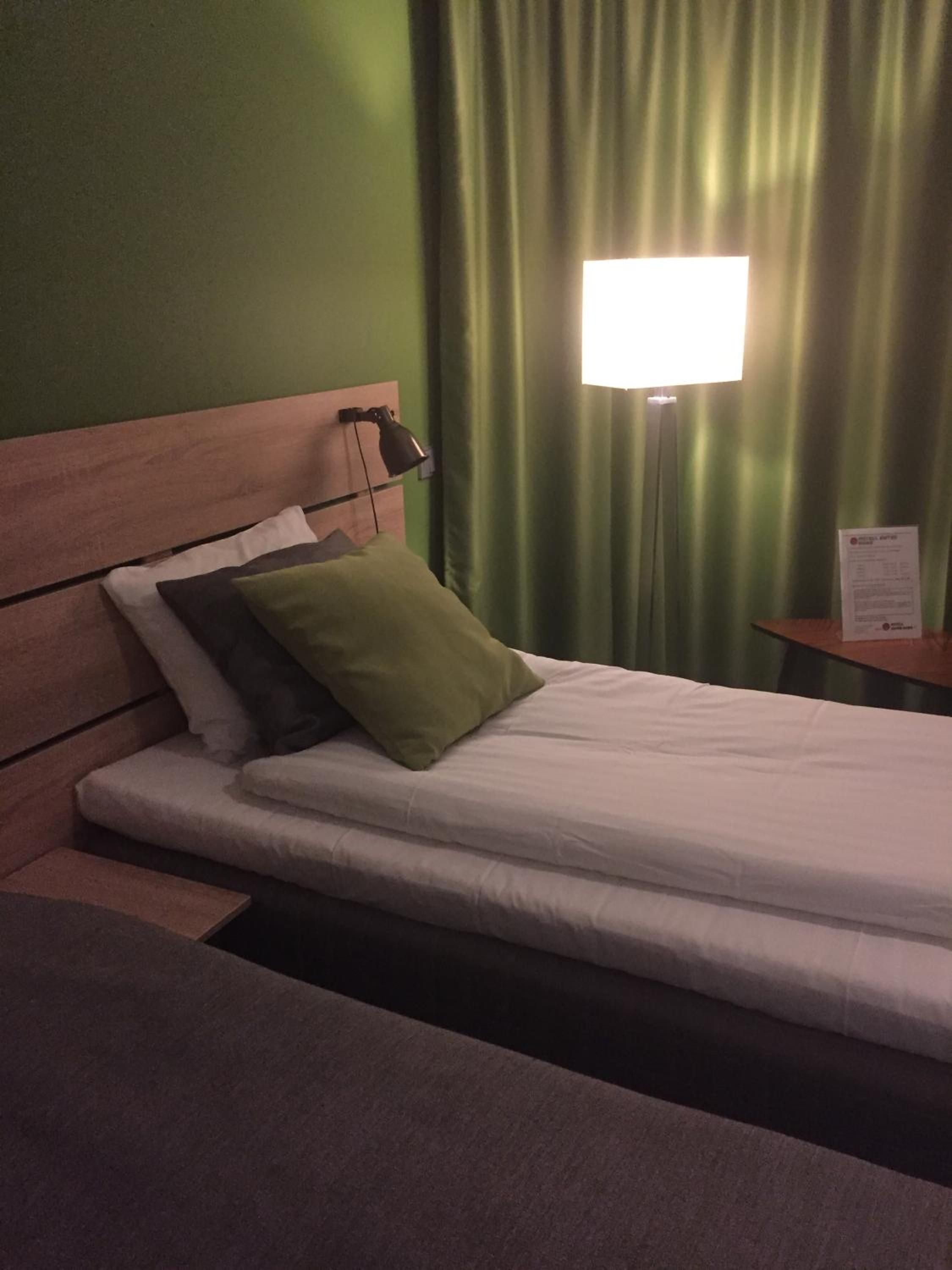 Ein Hotelzimmer mit einem Bett, einem Nachttisch, einer Lampe und einem grünen Vorhang.