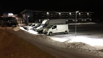 A parking area with several vehicles, including a white van, and a building with multiple windows in the background.