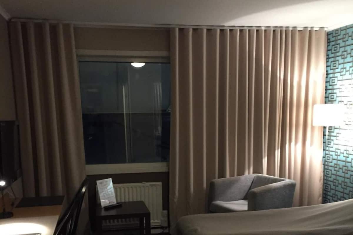 A hotel room with two single beds, a desk with a chair, a small table, and a window with curtains.