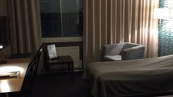 Habitación de hotel con dos camas individuales, un escritorio con silla, una mesita y una ventana con cortinas.