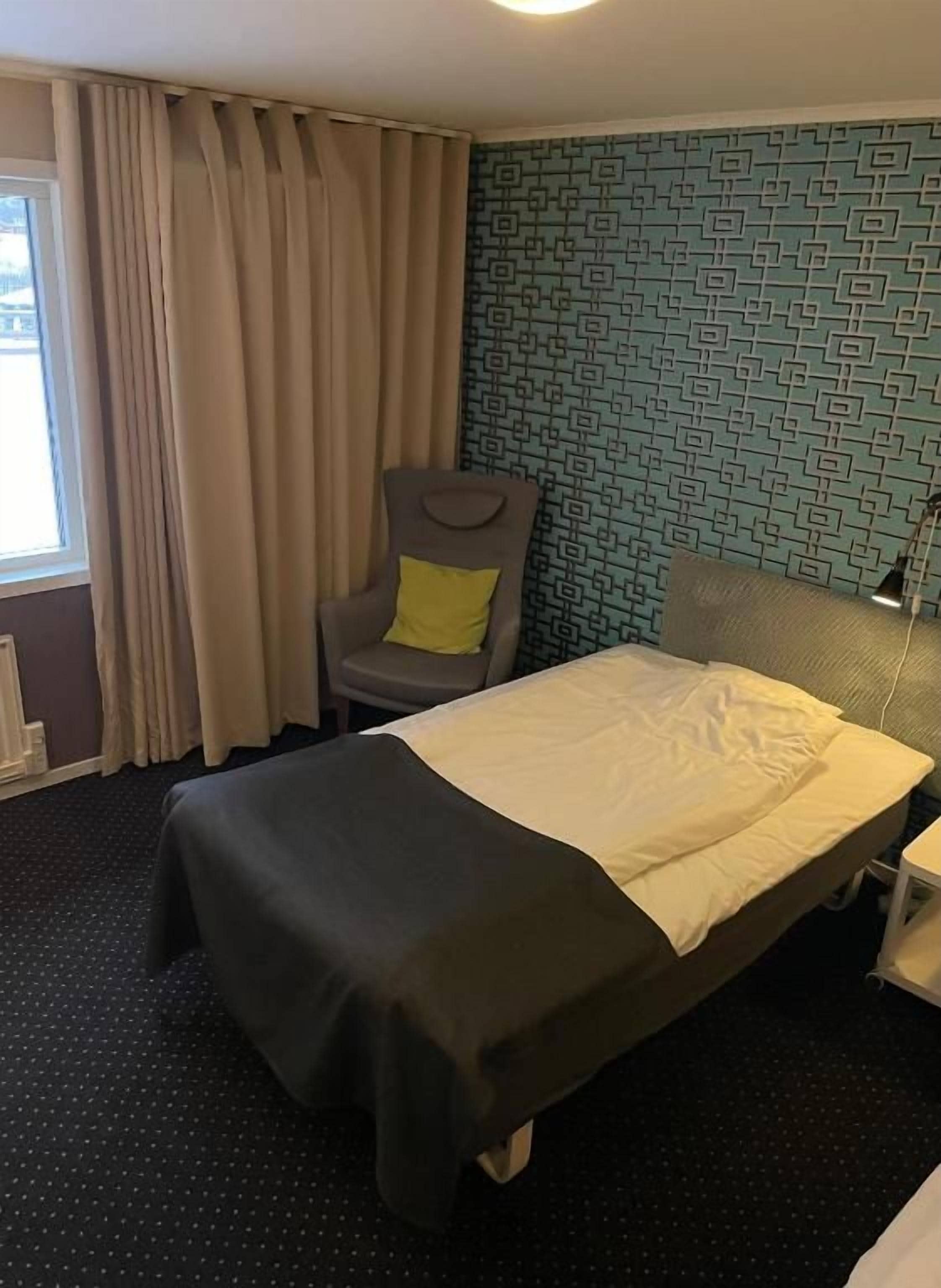 Quarto de hotel com cama, cadeira, escrivaninha e parede estampada.