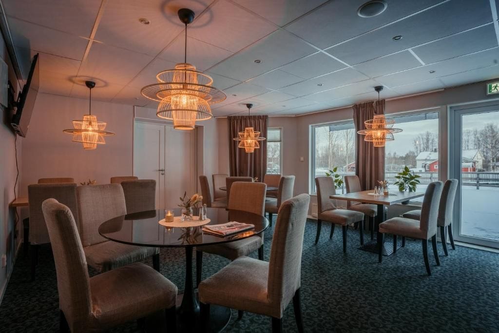 A hotel dining area with round tables, chairs, and pendant lighting.