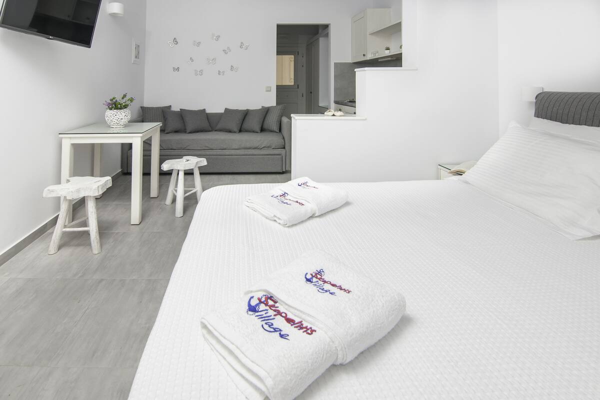A modern hotel room with a bed, a gray sofa, a small table, and a TV mounted on the wall.