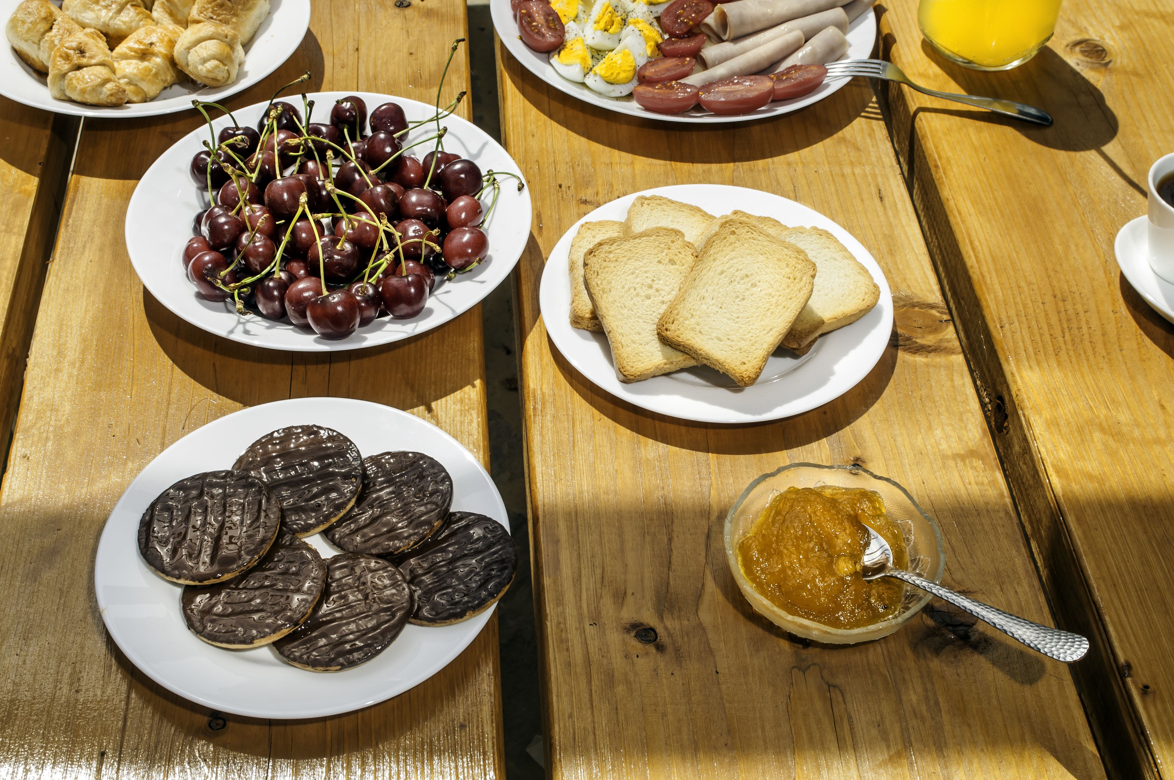 A wooden table with plates of food including cherries, toast, and chocolate cookies.