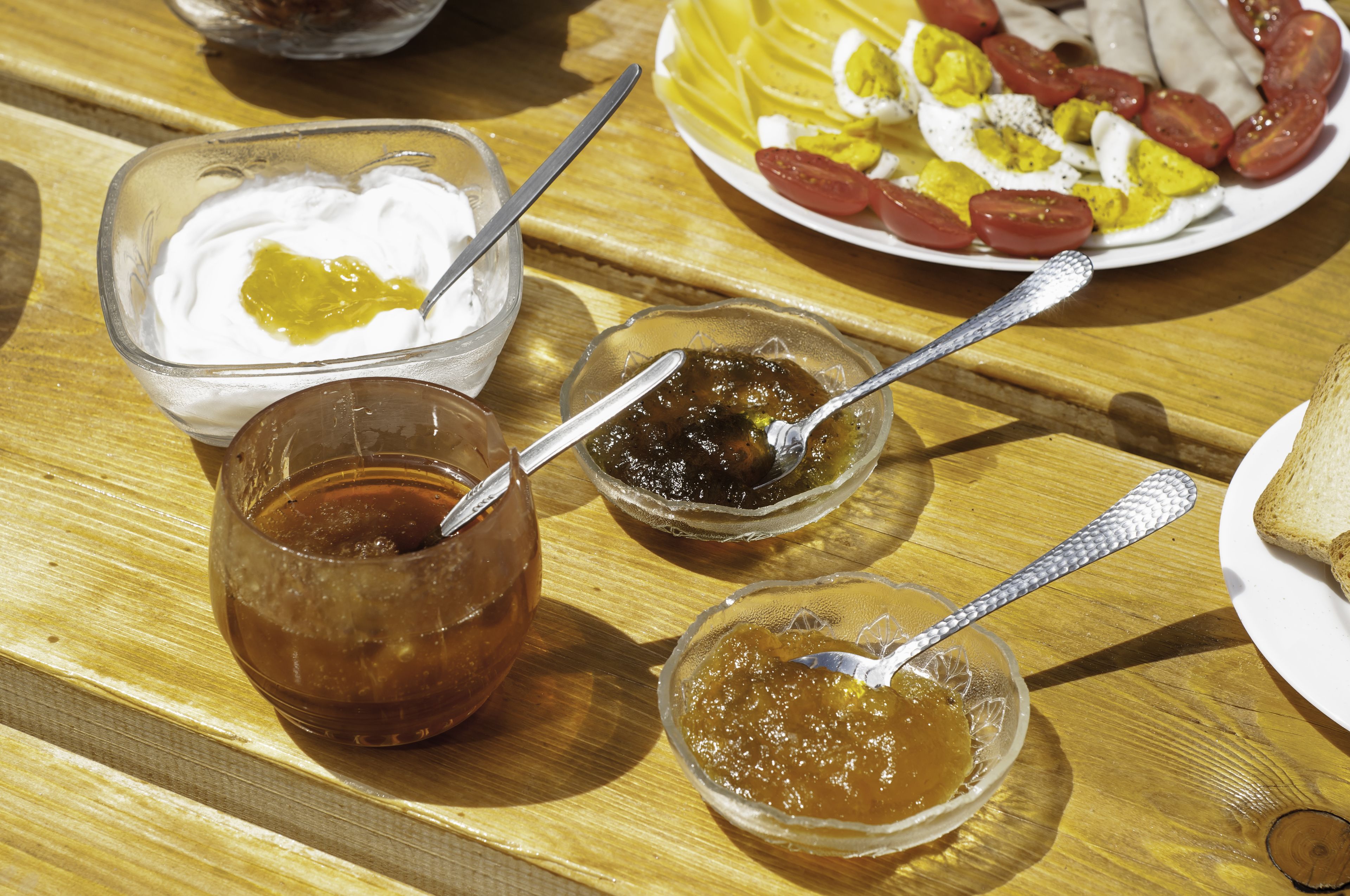 A wooden table with four glass bowls containing different condiments, a plate of eggs, and sausages.
