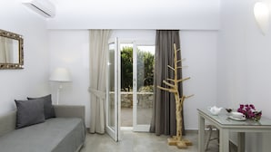A room with a sofa, a table with a teapot and flowers, a mirror, and a view through a glass door. - Skopelitis Village (Amorgos)