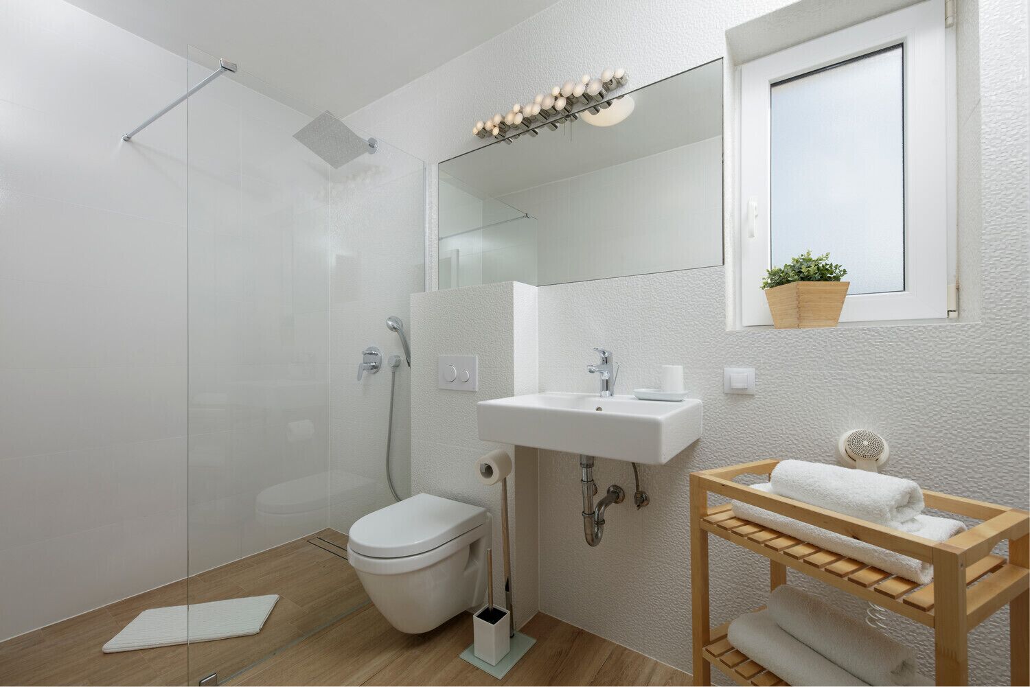 A modern bathroom with a glass shower enclosure, a white toilet, a sink with a mirror above, and a wooden vanity with a towel rack.