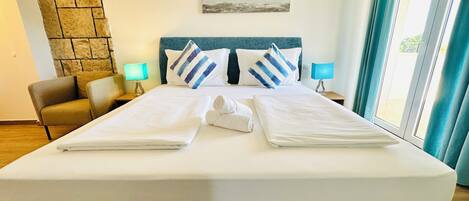 A hotel room with a large bed, two bedside tables, a chair, a stone wall, and a painting of the sea.