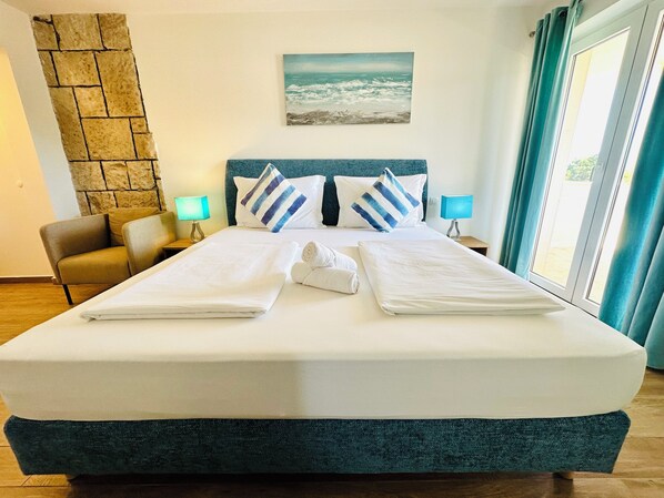 A hotel room with a large bed, two bedside tables, a chair, a stone wall, and a painting of the sea. - Villa Mediterranea (Bol)