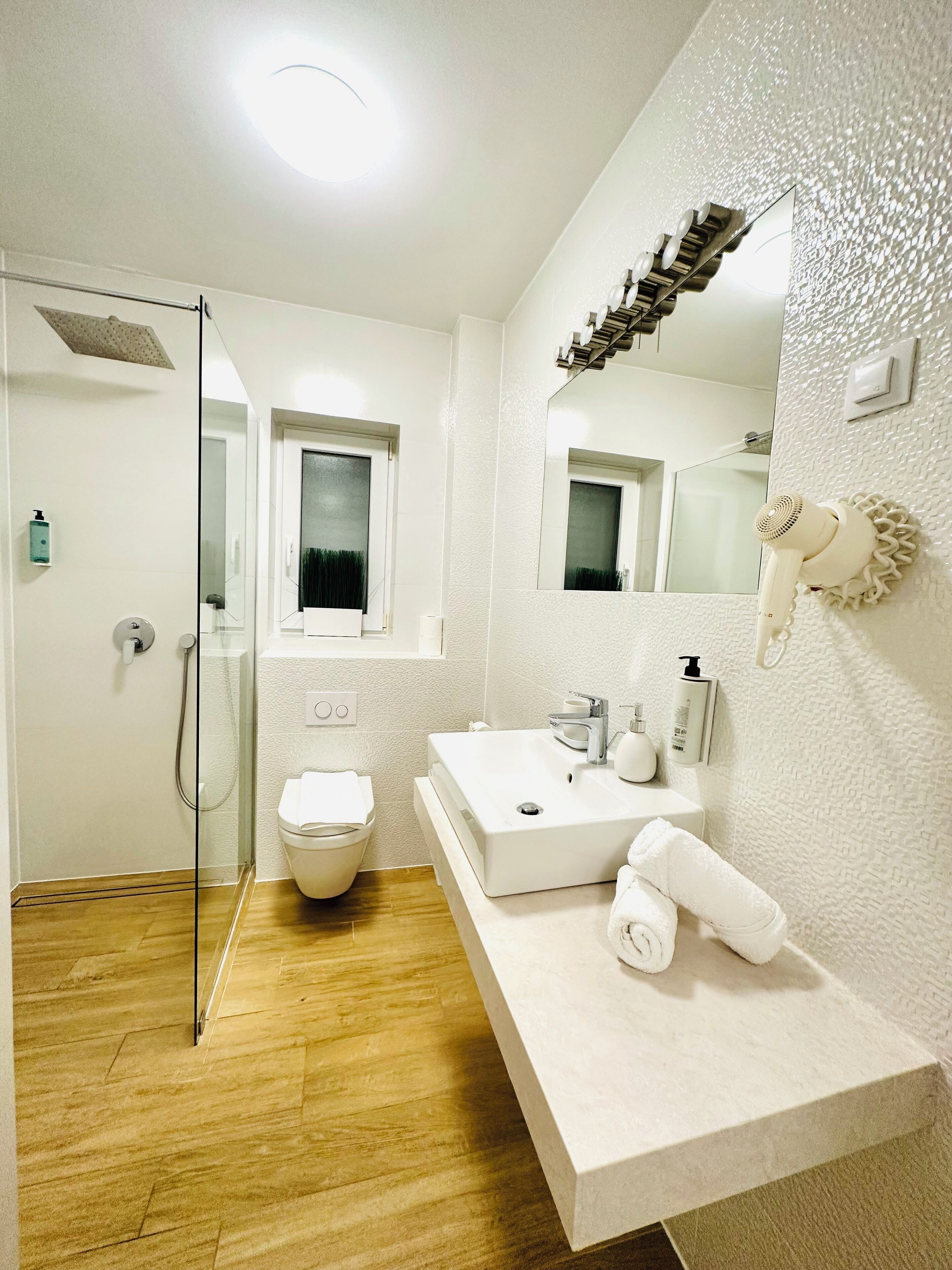 A modern bathroom with a glass shower enclosure, a white sink with a vanity, and a large mirror.