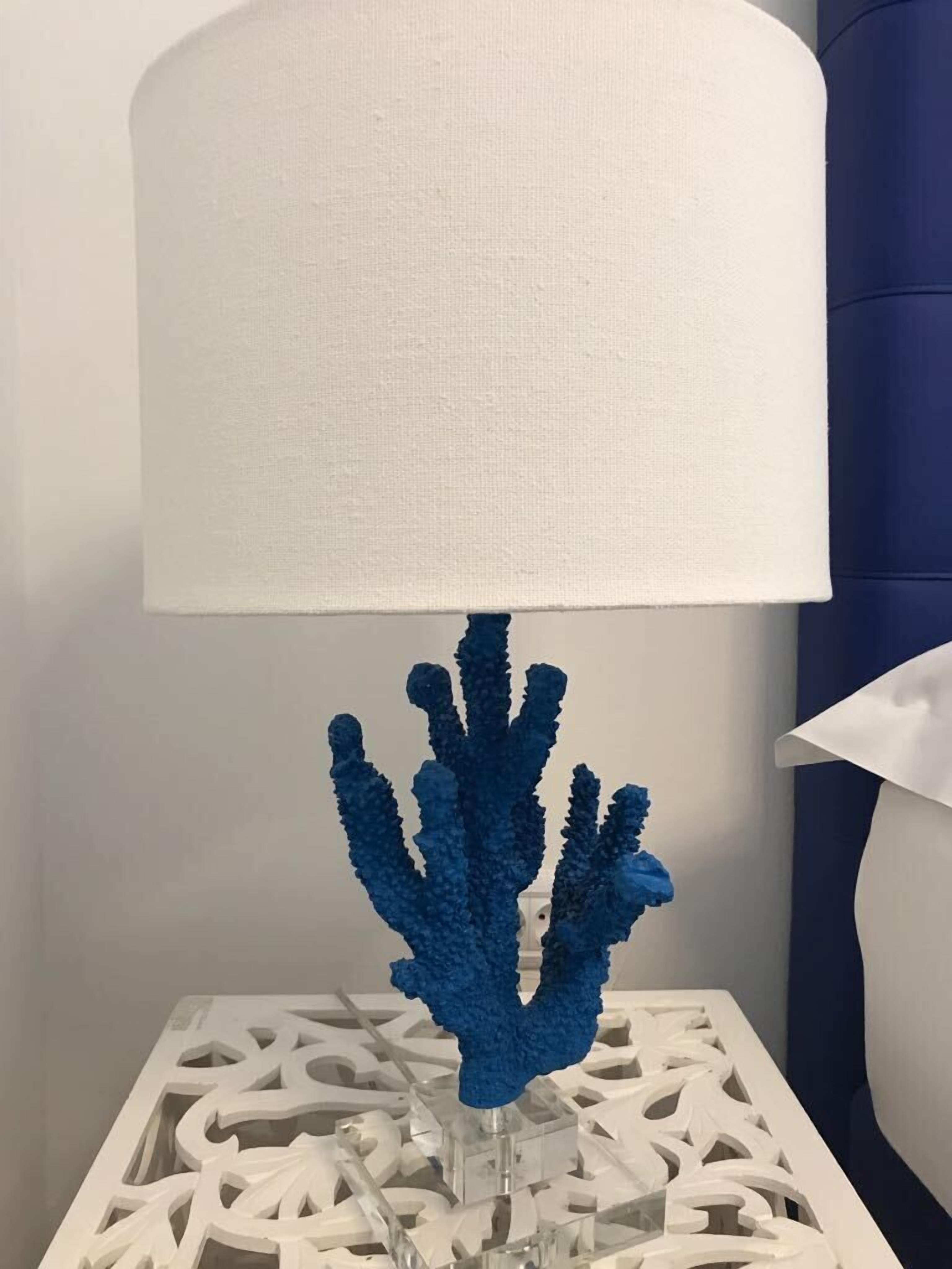 A white table lamp with a blue coral-like base on a white, intricately patterned table.