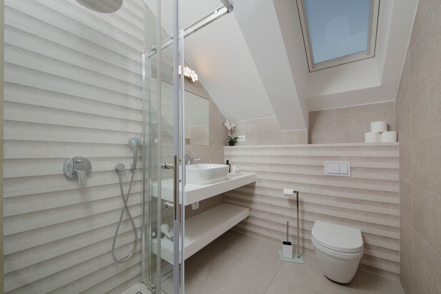 Une salle de bain moderne avec une douche à l’italienne en verre, un lavabo blanc et des toilettes.