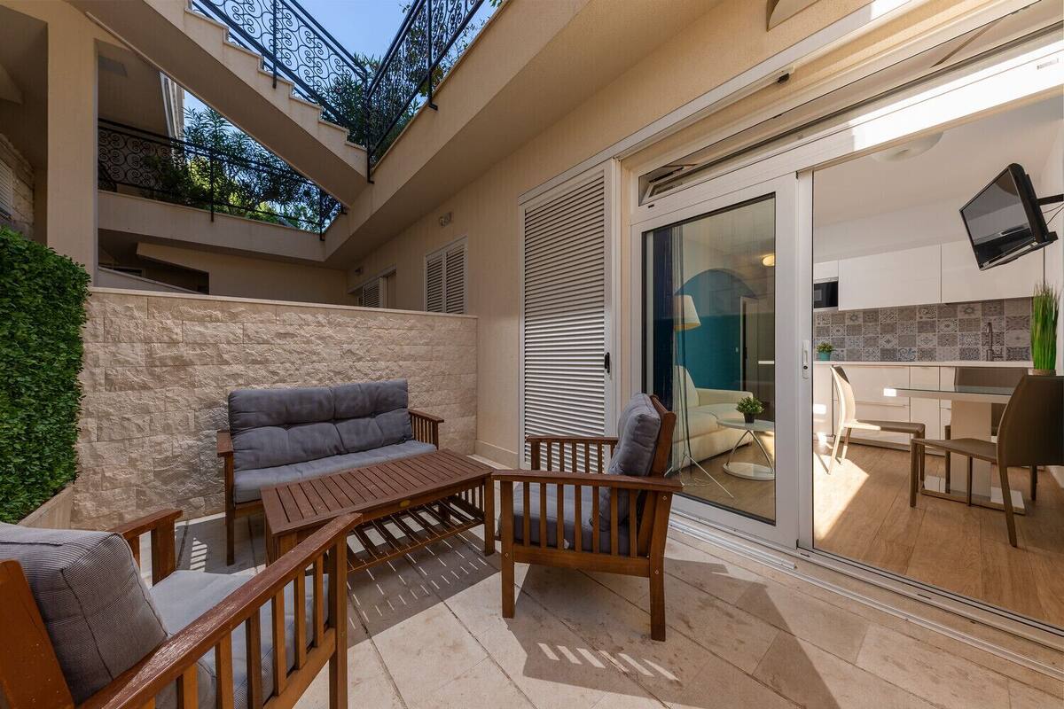A balcony with a sofa and chairs, a stone wall, and a view of the interior through a glass door.