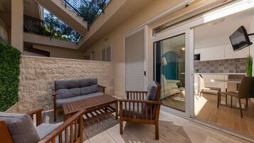Un balcon avec un canapé et des fauteuils, un mur en pierre et une vue sur l’intérieur, visible à travers une porte vitrée.
