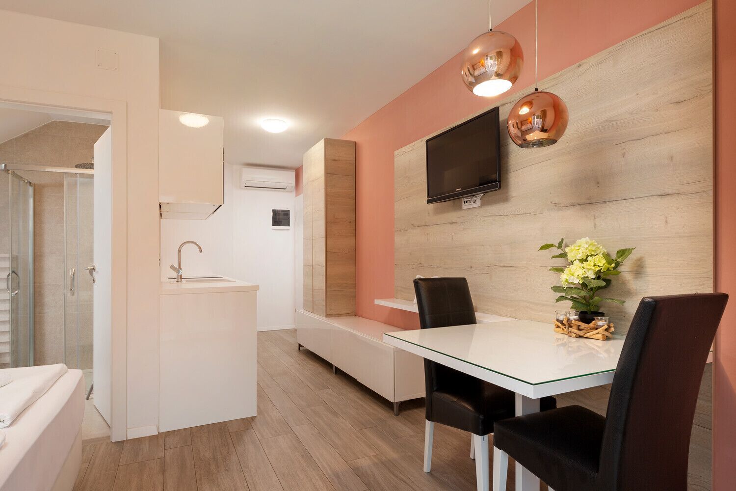 Una cocina moderna con horno integrado, un comedor con mesa de vidrio y un televisor montado en la pared.