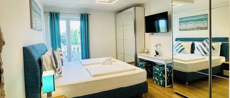 A modern hotel room with a large bed, a sofa, a TV, and a mirror.