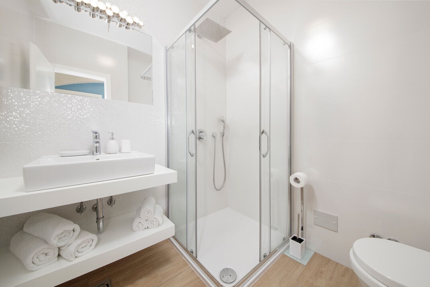 A modern bathroom with a glass-enclosed shower, a white sink with a mirror above it, and a toilet.