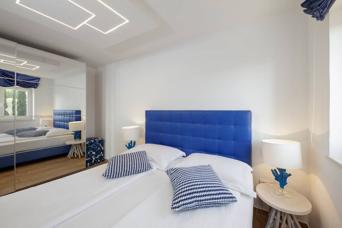 A modern hotel room with a large bed, a bedside table, a lamp, and a mirror.
